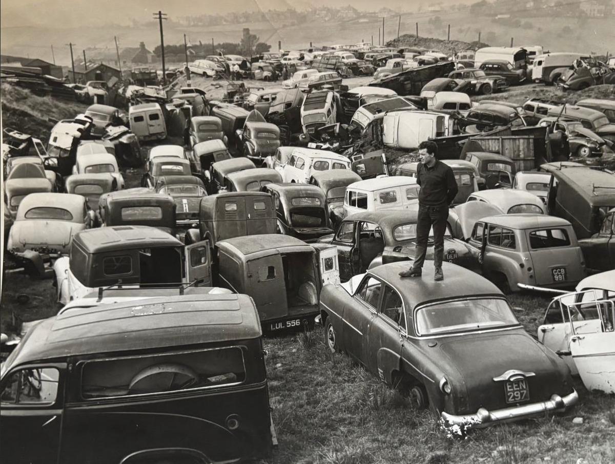 Adam Moffatt's grandfather standing on a stripped car in a 1950s scrap yard in the North of England